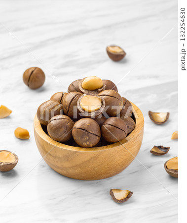 Macadamia nuts with shell in wood bowl with broken macadamia on marble table background Macadamia nuts with shell in wood bowl with broken macadamia on marble table background 132254630
