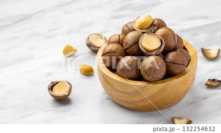 Macadamia nuts in wood bowl with broken macadamia on marble table background, closeup Macadamia nuts in wood bowl with broken macadamia on marble table background, closeup 132254632