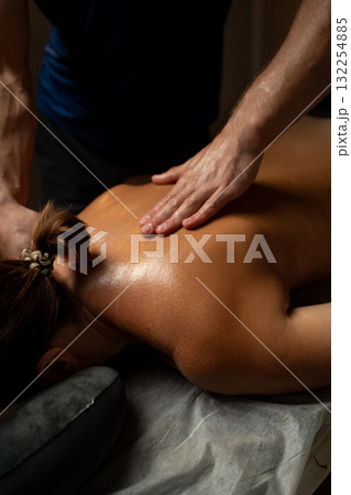 Close-up of a professional therapist performing a relaxing back massage in a spa setting, applying oil and pressure to relieve muscle tension and promote relaxation and wellbeing. Close-up of a professional therapist performing a relaxing back massage in a spa setting, applying oil and pressure to relieve muscle tension and promote relaxation and wellbeing. 132254885