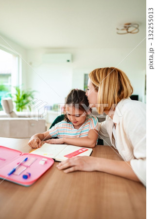 Mom helping daughter with homework in cozy home setting Mom helping daughter with homework in cozy home setting 132255013