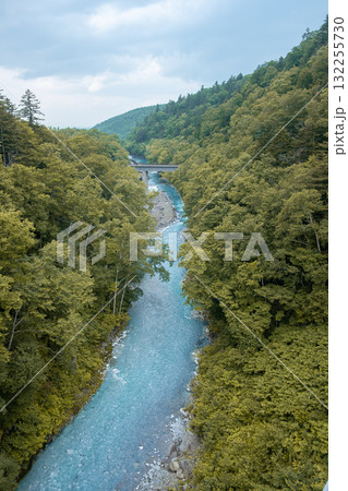 Clear Biei river flowing through dense forest with bridge in mountainous landscape view from Shirogane Bridge at Hokkaido, Japan 132255730