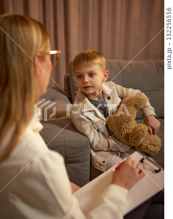 Boy holding teddy bear during therapy conversation with psychologist in calm atmosphere 132256556