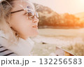 Woman Sunglasses Beach Sunset - A young woman wearing sunglasses gazes at the sunset over a beach. 132256583