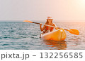 Kayaking Woman Ocean Sunset - Woman kayaking on calm ocean water at sunset. 132256585