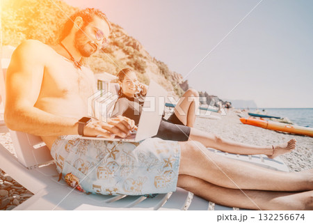 Beach Laptop Work Couple - Man and woman work on laptop while relaxing on beach chairs. 132256674
