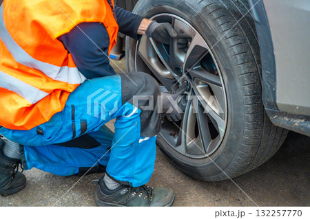 Mechanic removing a car wheel during seasonal tire change at an auto service shop. Timely winter tire replacement ensures road safety and compliance with regulations. 132257770