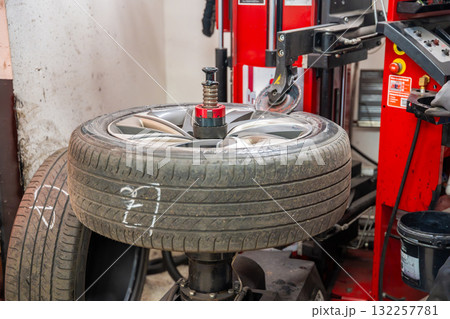 Tire changing machine removing the rubber tire from the rim using a rotating metal arm. Essential step in seasonal wheel replacement at a professional auto workshop. Tire changing machine removing the rubber tire from the rim using a rotating metal arm. Essential step in seasonal wheel replacement at a professional auto workshop. 132257781