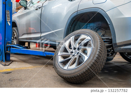 Prepared car wheel lying next to the vehicle before final installation. Seasonal tire change process during winter preparation at auto service workshop. Prepared car wheel lying next to the vehicle before final installation. Seasonal tire change process during winter preparation at auto service workshop. 132257782