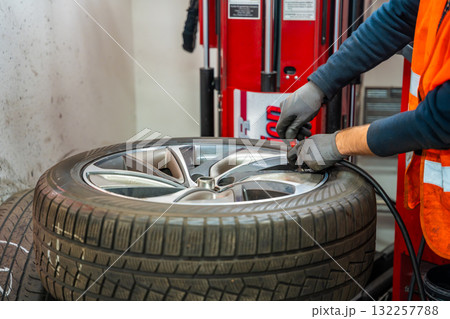 Inflating a car tire on a tire changing machine during seasonal wheel replacement. Critical step for proper pressure and road safety before winter driving. Inflating a car tire on a tire changing machine during seasonal wheel replacement. Critical step for proper pressure and road safety before winter driving. 132257788