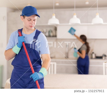 Young boy in blue uniform cleaning the floor in the kitchen Young boy in blue uniform cleaning the floor in the kitchen 132257911