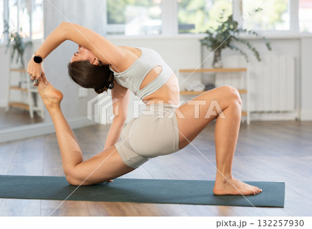 Young woman performing Baddha Anjaneyasana in yoga studio 132257930