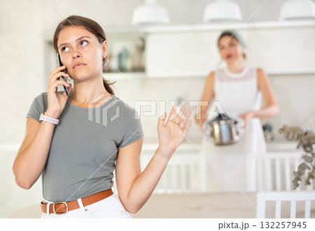Young girl standing at the table while woman is quarreling with her standing behind 132257945