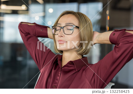 Businesswoman taking a mindful break, meditating to relieve stress, relaxing in an office chair with closed eyes and hands behind head, finding peace during a busy day Businesswoman taking a mindful break, meditating to relieve stress, relaxing in an office chair with closed eyes and hands behind head, finding peace during a busy day 132258425