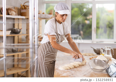 Elderly woman baker cutting dough with scraper 132258931