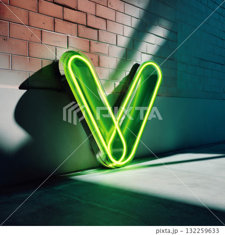 A large neon sign with the letter V in a bold, sans-serif font, set against a brick wall backdrop. The lighting is soft and diffused, casting gentle shadows on the ground below the sign. 132259633