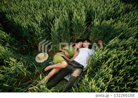 Couple is lying down on the agricultural field with high wheat that is growing 132260108