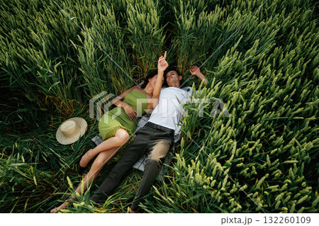 Couple is lying down on the agricultural field with high wheat that is growing Couple is lying down on the agricultural field with high wheat that is growing 132260109