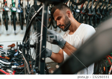 In grey colored gloves. Repair man in bicycle shop, working in store 132260331