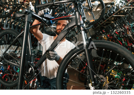 In grey colored gloves. Repair man in bicycle shop, working in store In grey colored gloves. Repair man in bicycle shop, working in store 132260335