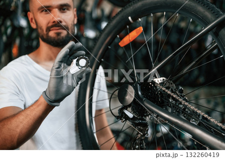Holding circle shaped part near the wheel. Repair man in bicycle shop, working in store Holding circle shaped part near the wheel. Repair man in bicycle shop, working in store 132260419