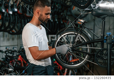 Indoors, many bikes. Repair man in bicycle shop, working in store Indoors, many bikes. Repair man in bicycle shop, working in store 132260435