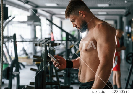 With smartphone, taking a break. Strong muscular man is working out in the gym With smartphone, taking a break. Strong muscular man is working out in the gym 132260550