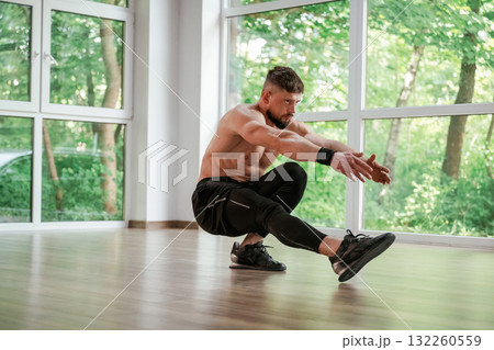 Daytime, trees outside the windows. Strong muscular man is working out in the gym 132260559