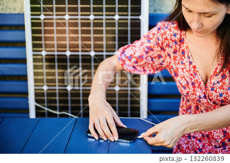 Pretty woman using portable solar battery to charge phone. Young female putting her mobile device on charge from solar panel. Sustainable lifestyle and green energy concept. 132260839