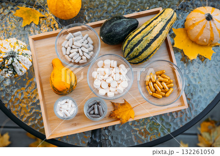Outdoor flatlay of fall gourds and various supplements in glass bowls arranged on a wooden tray over autumn leaves. Functional nutrition in natural contexts, whole food supplements, seasonal wellness 132261050