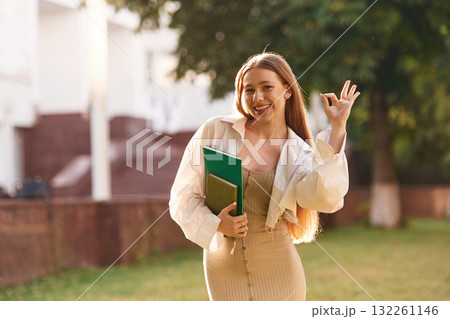 With notepads. Beautiful female student is outdoors near the university With notepads. Beautiful female student is outdoors near the university 132261146