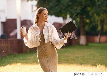 Digital tablet and cup of drink in hands. Beautiful female student is outdoors near the university Digital tablet and cup of drink in hands. Beautiful female student is outdoors near the university 132261148