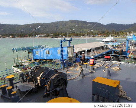 Ferry Docked at a Coastal Pier with Crew on Deck and Mountains in the Background 132261185