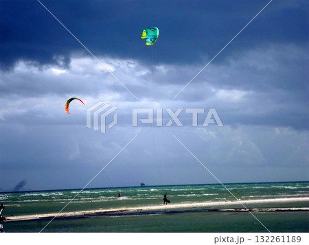 Kitesurfers Soaring Over Coastal Waters Under a Cloudy Sky on a Windy Day 132261189