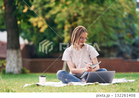 On the grass with laptop. Beautiful female student is outdoors near the university 132261408