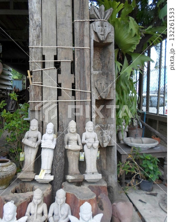 A Weathered Wooden Wall Adorned with Stone Statues and Lush Plants in an Outdoor Market 132261533