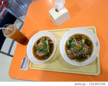 A Flavorful Noodle Soup Meal with Iced Tea on an Orange Table in a Casual Dining Setting 132261540