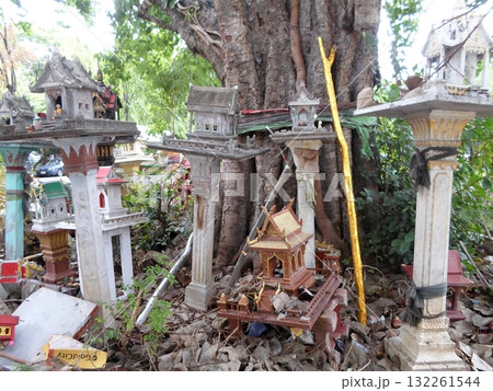 Cluster of Thai Spirit Houses Around a Tree with a Golden Stick and Offerings 132261544