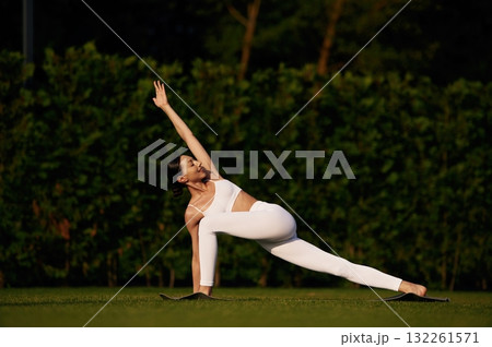 Doing yoga exercises. Attractive young fitness woman is on the green grass at daytime Doing yoga exercises. Attractive young fitness woman is on the green grass at daytime 132261571