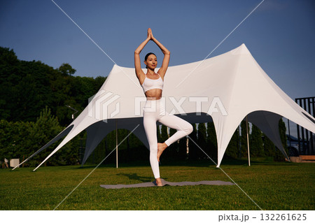 Doing yoga exercises. Attractive young fitness woman is on the green grass at daytime 132261625