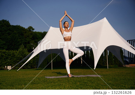 Doing yoga exercises. Attractive young fitness woman is on the green grass at daytime 132261626