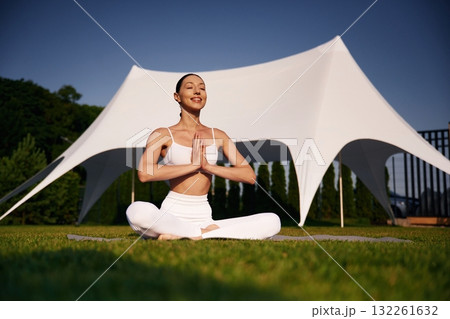 Sitting in the lotus pose. Attractive young fitness woman is on the green grass at daytime Sitting in the lotus pose. Attractive young fitness woman is on the green grass at daytime 132261632