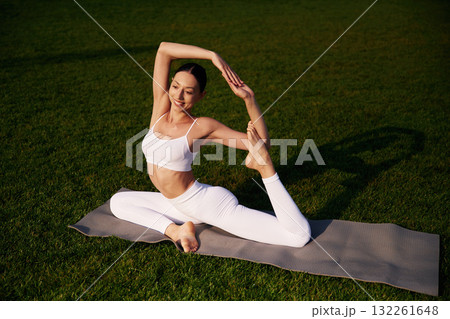 Exercises for flexibility. Attractive young fitness woman is on the green grass at daytime 132261648