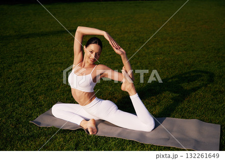 On the yoga mat, exercises. Attractive young fitness woman is on the green grass at daytime On the yoga mat, exercises. Attractive young fitness woman is on the green grass at daytime 132261649
