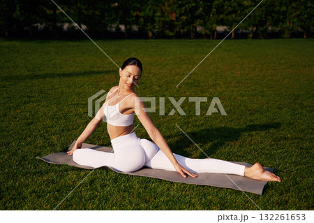 On the yoga mat, exercises. Attractive young fitness woman is on the green grass at daytime 132261653