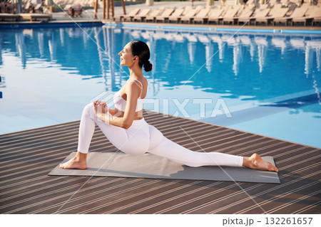Busy by doing yoga exercise. Fitness woman is near the pool Busy by doing yoga exercise. Fitness woman is near the pool 132261657
