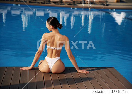 Back view, sitting. Beautiful woman in bikini is resting by the pool 132261733