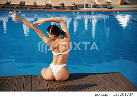 Back view, sitting. Beautiful woman in bikini is resting by the pool Back view, sitting. Beautiful woman in bikini is resting by the pool 132261734