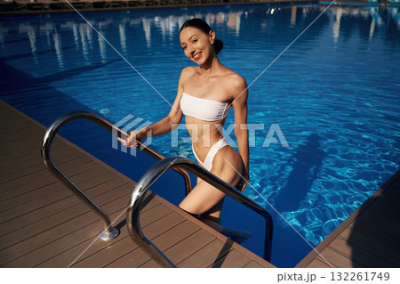 Going up out the water. Beautiful woman in bikini is resting by the pool 132261749