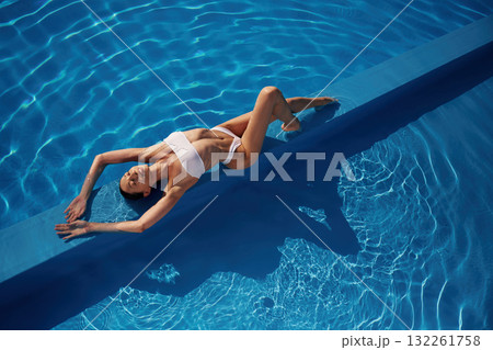 View from the top, lying down. Beautiful woman in bikini is resting by the pool View from the top, lying down. Beautiful woman in bikini is resting by the pool 132261758