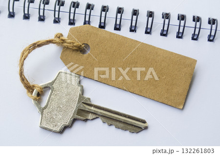 A silver key placed beside a brown cardboard tag on a spiral notebook representing access credentials, password reminder and personal security concept. 132261803